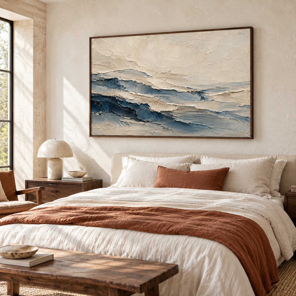 Cream and blue abstract painting above a low bed with white linen, viewed from the left near the foot of the bed in a bright bedroom.
