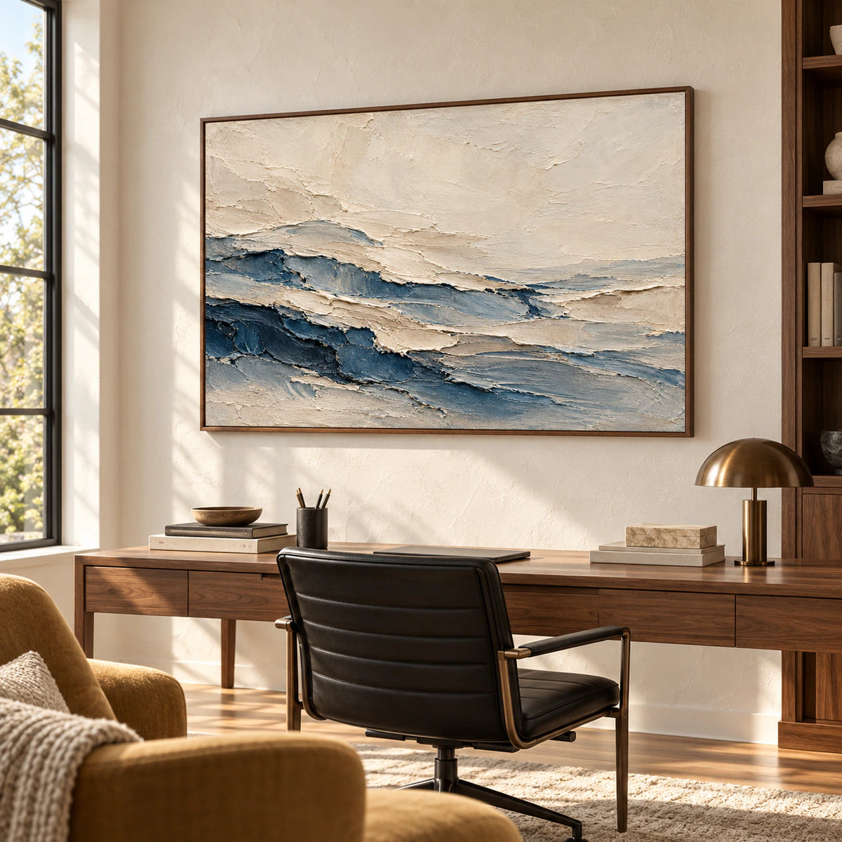 Large horizontal abstract painting above a warm wood desk, viewed from the right in a bright office with a black desk chair and ochre reading chair.