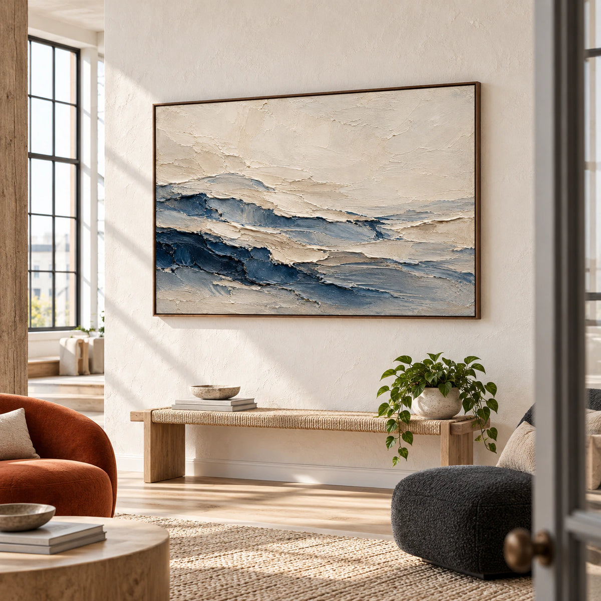 Horizontal cream and blue abstract painting on a warm-white wall, viewed from the right in an airy loft with tall windows, a charcoal chair and pale oak bench.