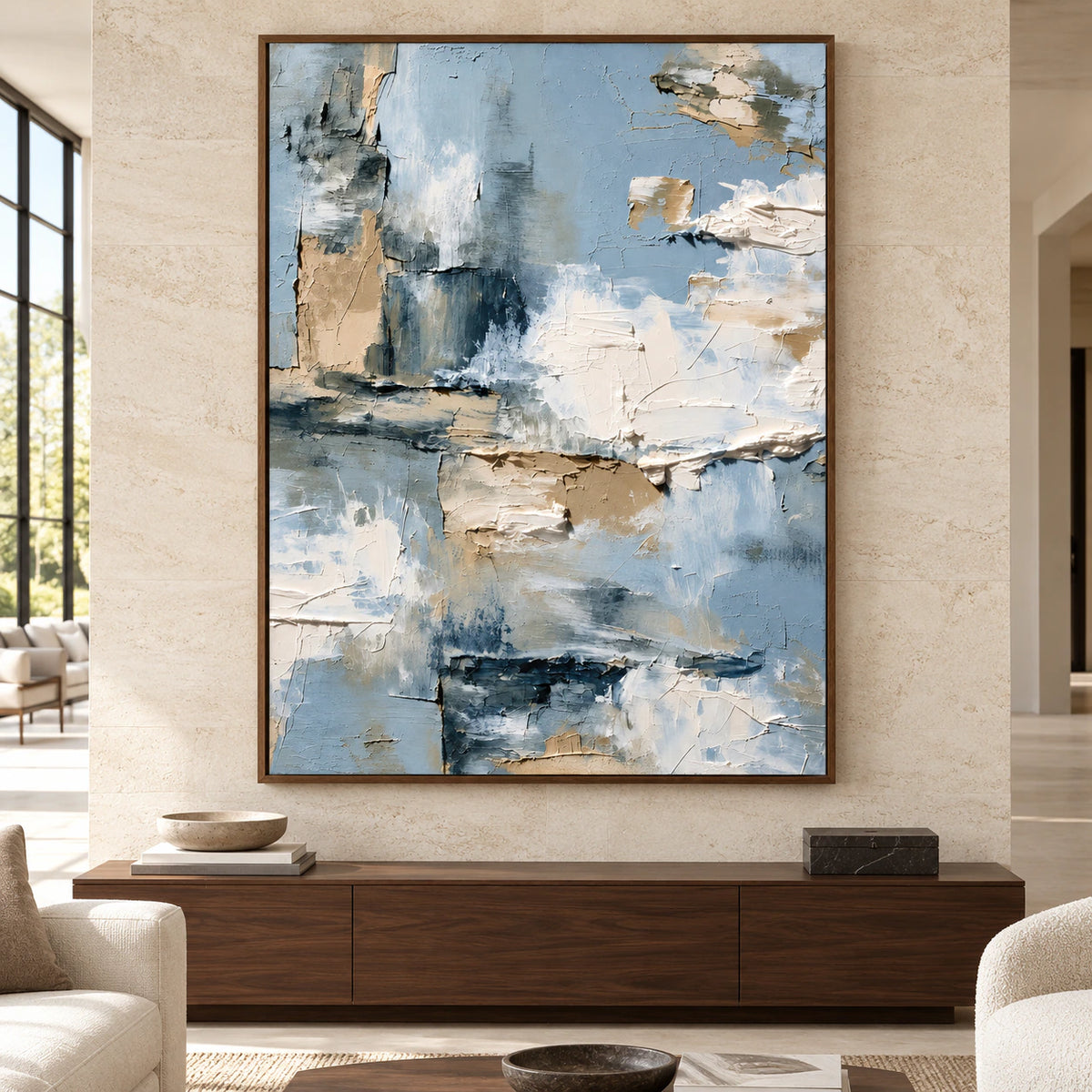 Large vertical abstract painting with raised cream, sand and blue-grey forms above a low console in a bright, spacious living room.