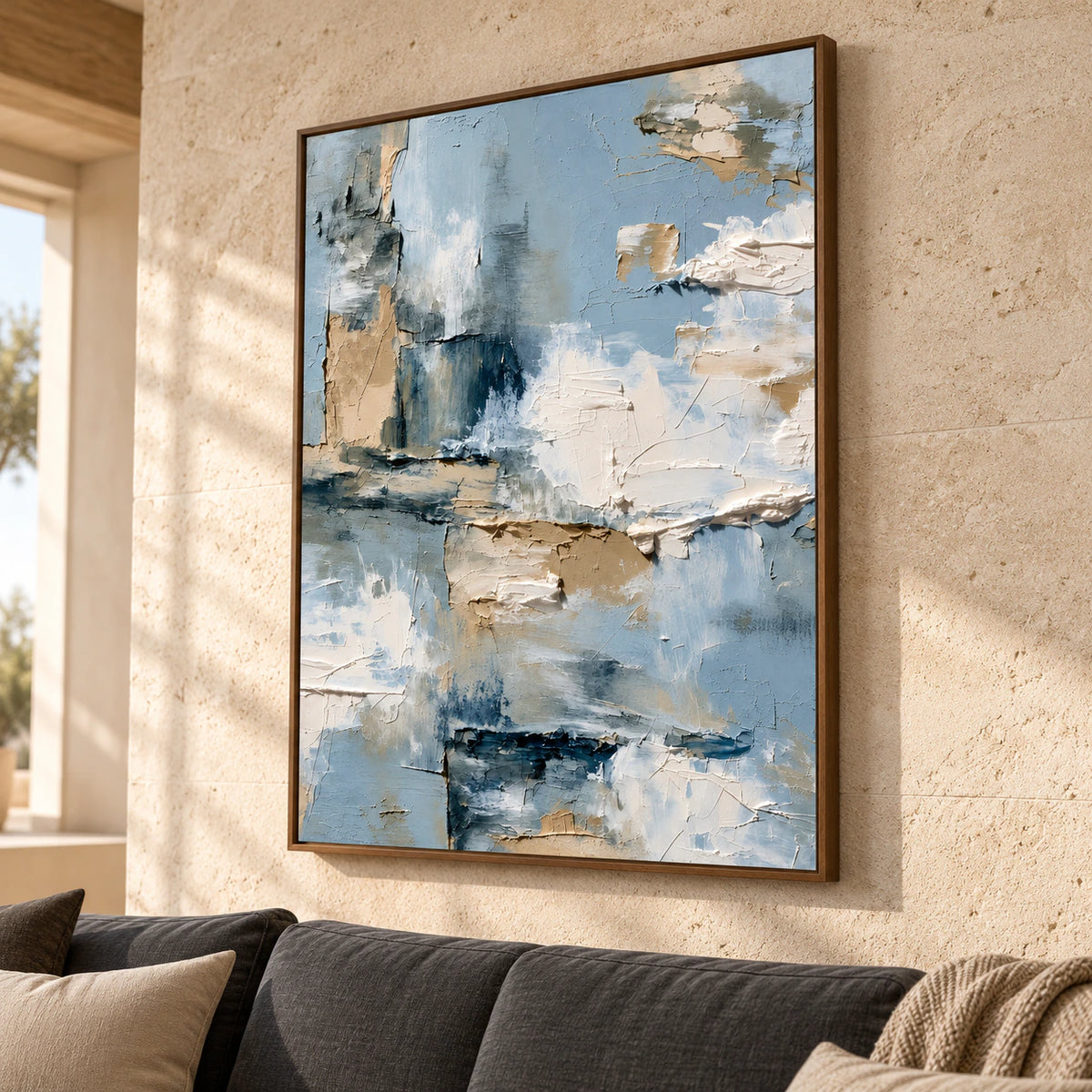 Large vertical abstract painting above a restrained charcoal sofa in a bright living room, its layered cream and blue-grey surface clearly visible.
