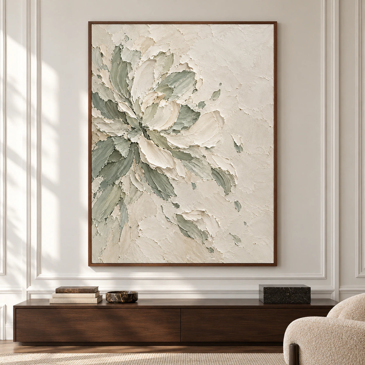 Large vertical floral artwork with ivory petals and sage-gray leaves centered on a pale wall in a spacious, sunlit room.