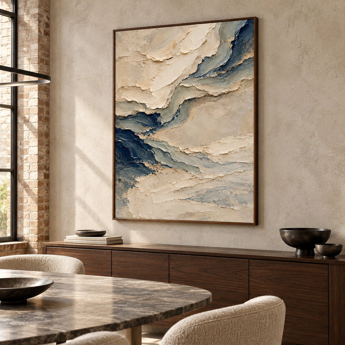 Pale-Undertow above a dark walnut sideboard, viewed from the right in a daylight-filled dining room with a pale stone wall and sculptural dining table.
