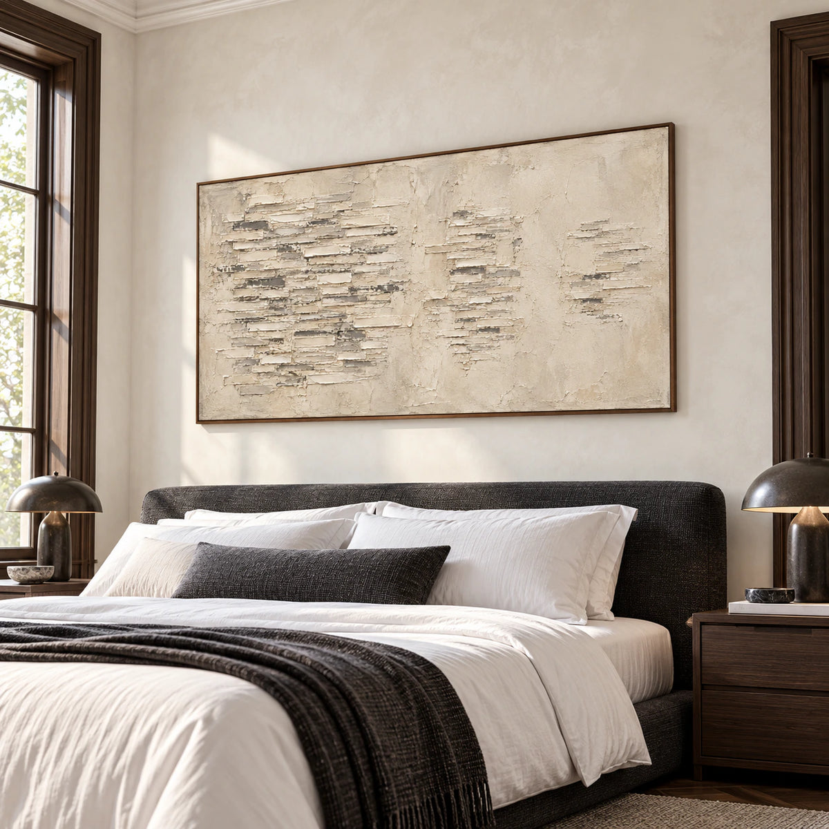 Wide parchment-toned abstract painting with layered pale ridges above a low charcoal upholstered bed in a quiet bright bedroom.