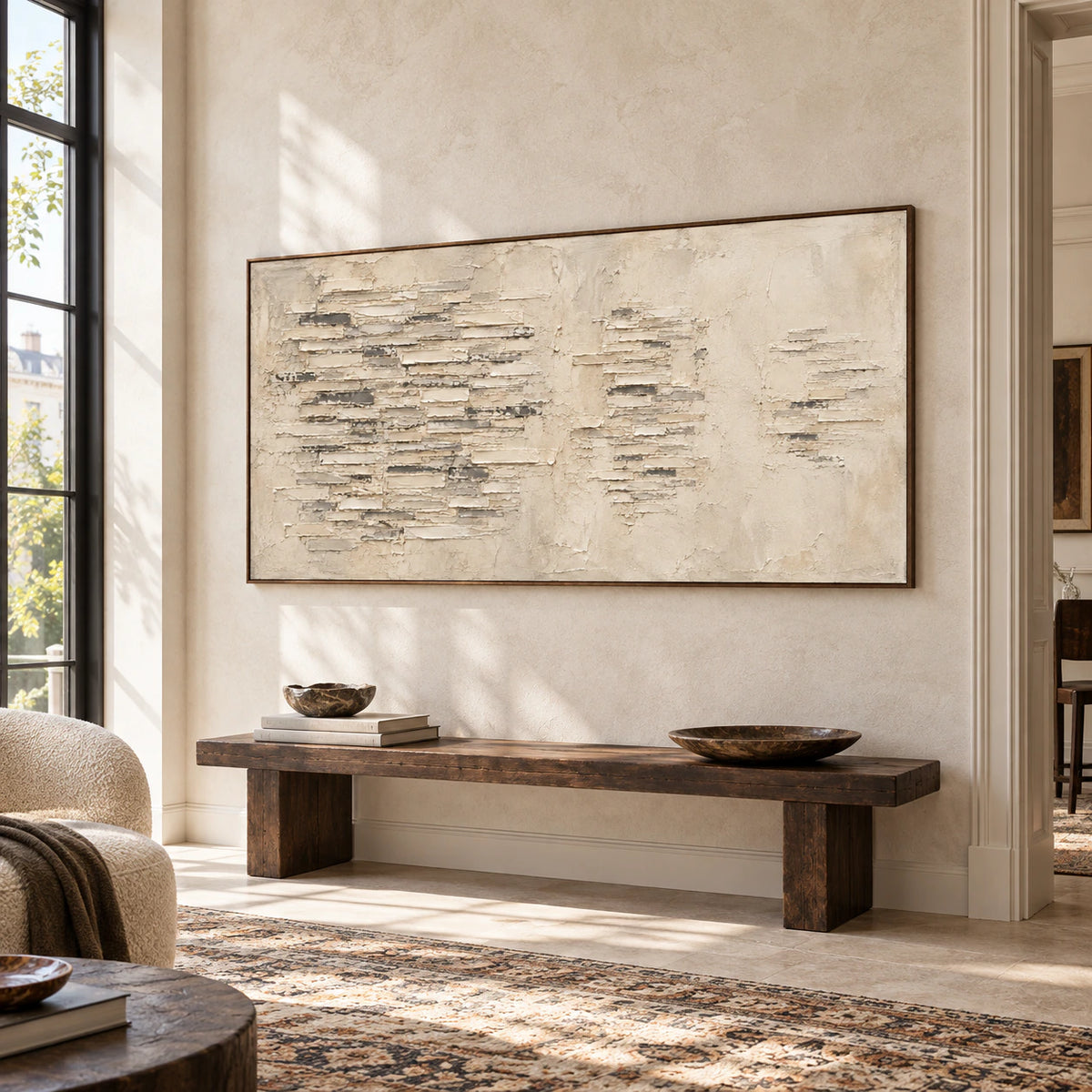 Large ivory and gray relief-like abstract painting anchoring a bright gallery-scale foyer with limestone walls and a dark wood bench.