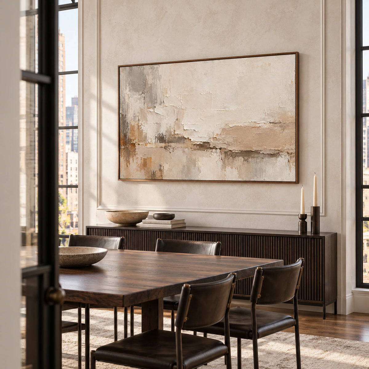 Large horizontal artwork on a light dining room wall above a long dark wood table, with daylight falling across the textured surface.