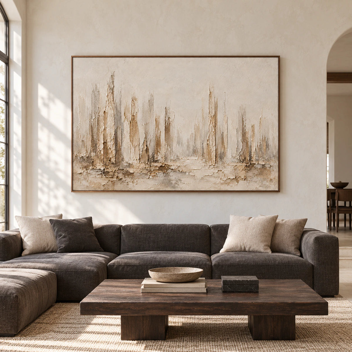 Large horizontal ivory and taupe abstract painting viewed straight on against a broad pale plaster wall, with dark wood and charcoal furnishings in natural daylight.