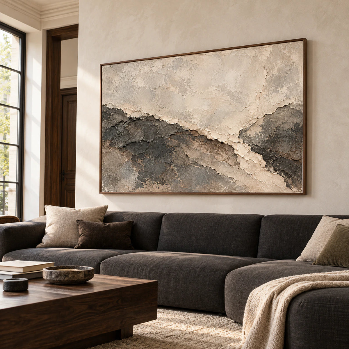Parchment Torrent hangs prominently above a low charcoal sofa in a bright living room with pale plaster walls and restrained furnishings.
