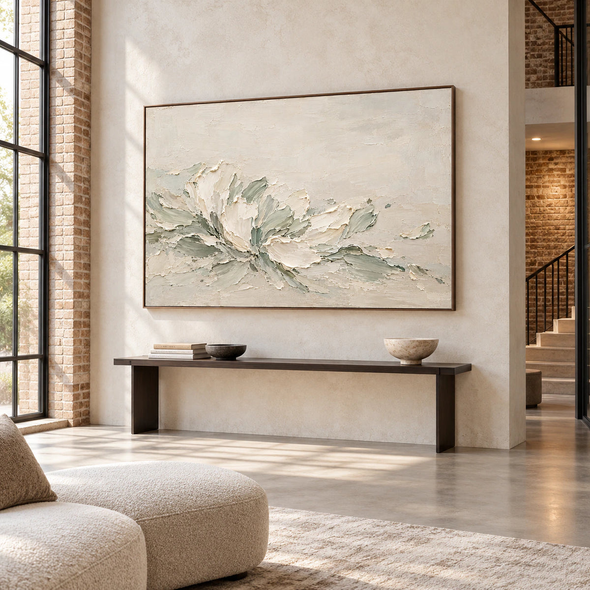 Ivory and sage abstract painting on a tall pale stone wall with a slim dark console in an open foyer, viewed from a low left angle.
