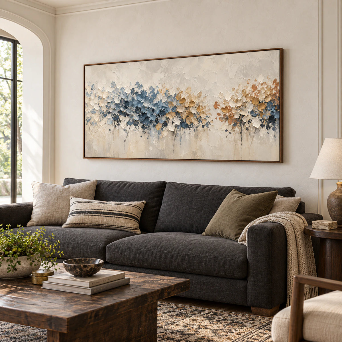 Petal-Passage above a charcoal linen sofa in a bright living room with pale plaster walls and a dark wood side table, viewed obliquely from the left.