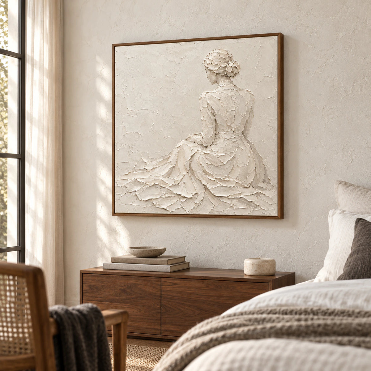 Ivory figure artwork above a low walnut bedside cabinet in a quiet, sunlit bedroom with crisp white linens.