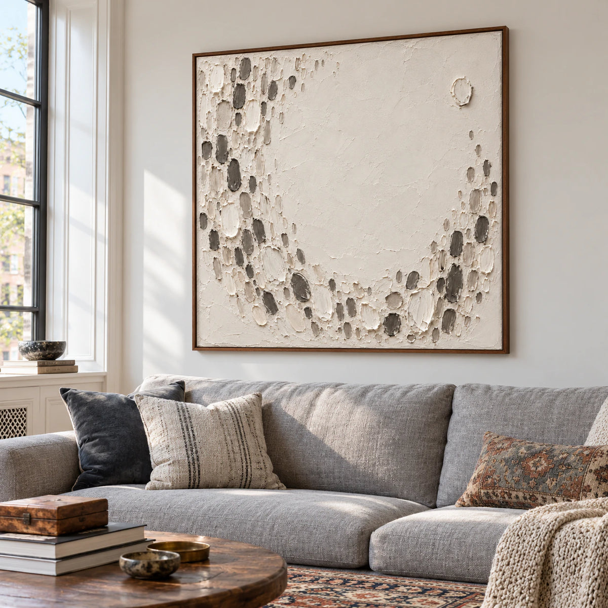 Square ivory and charcoal textured abstract above a restrained sofa in a bright living room.