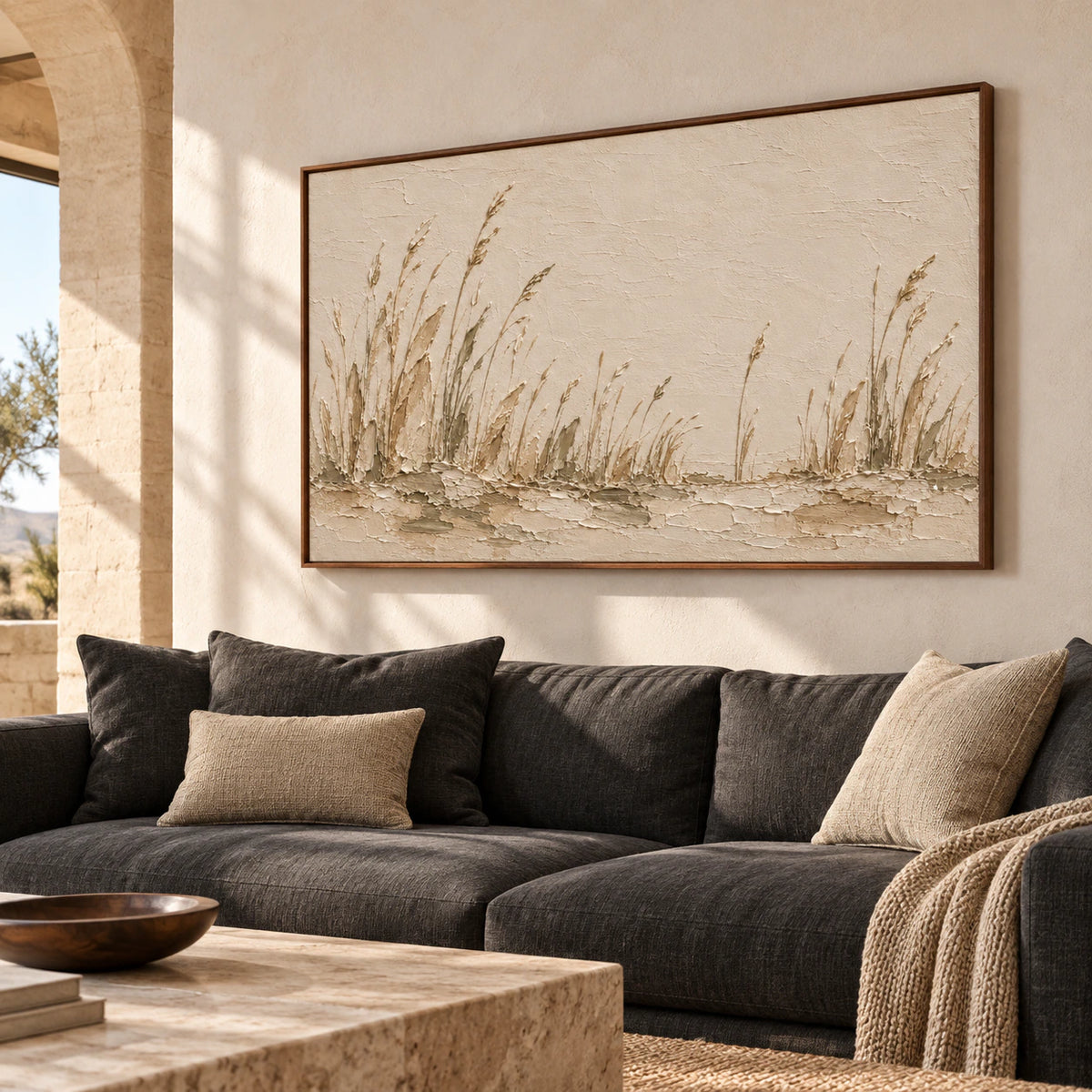 Left-oblique view of a large reed landscape above a charcoal gray sofa in a bright living room with pale plaster walls and walnut accents.