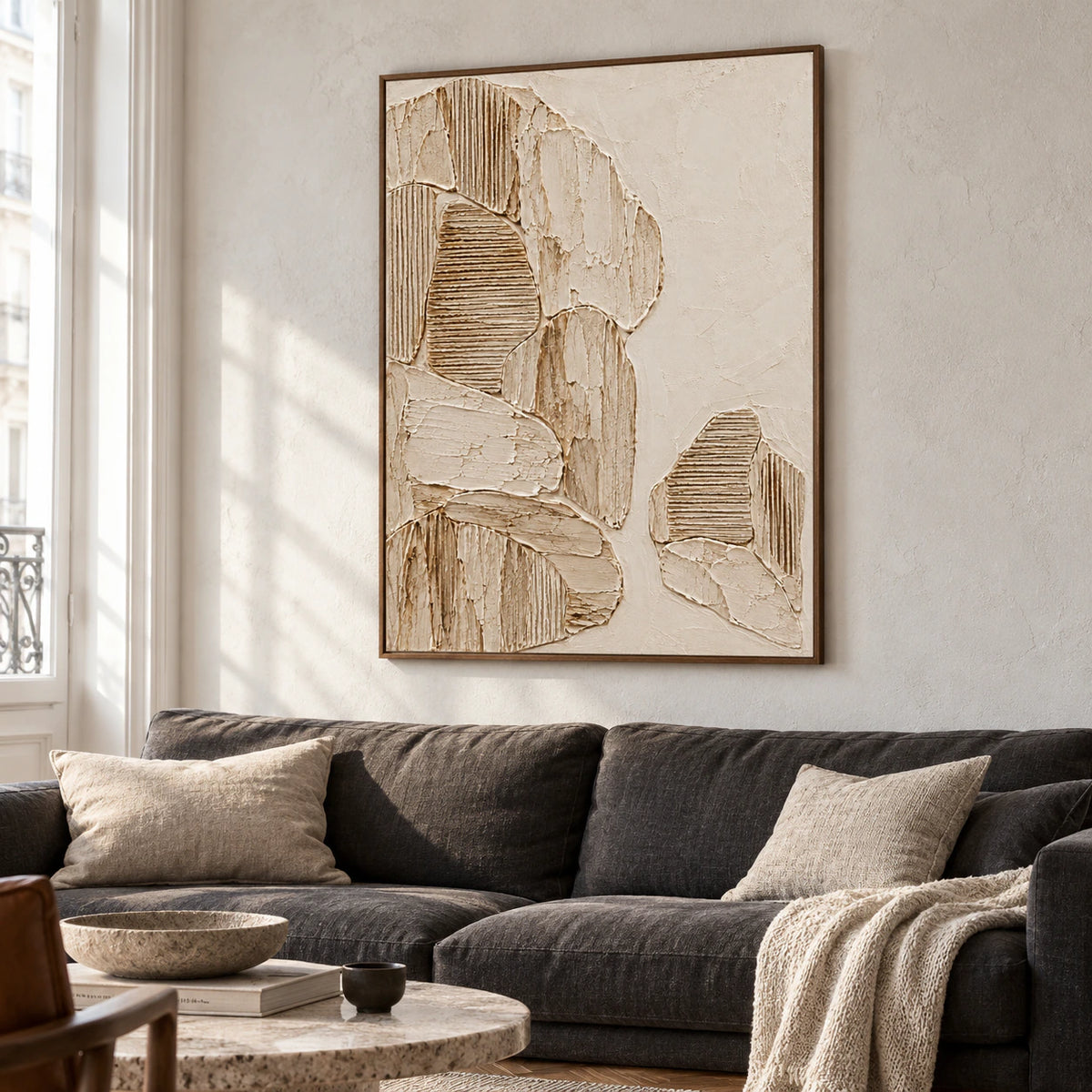 Large ribbed parchment artwork above a low charcoal sofa in a bright living room with pale walls and daylight from tall windows.