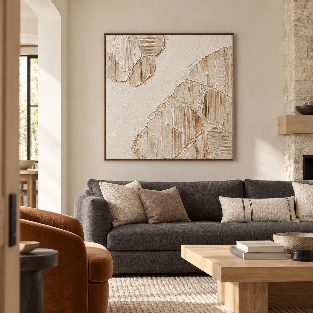 Large square ivory relief displayed above a charcoal linen sofa in a bright living room with pale stone walls.
