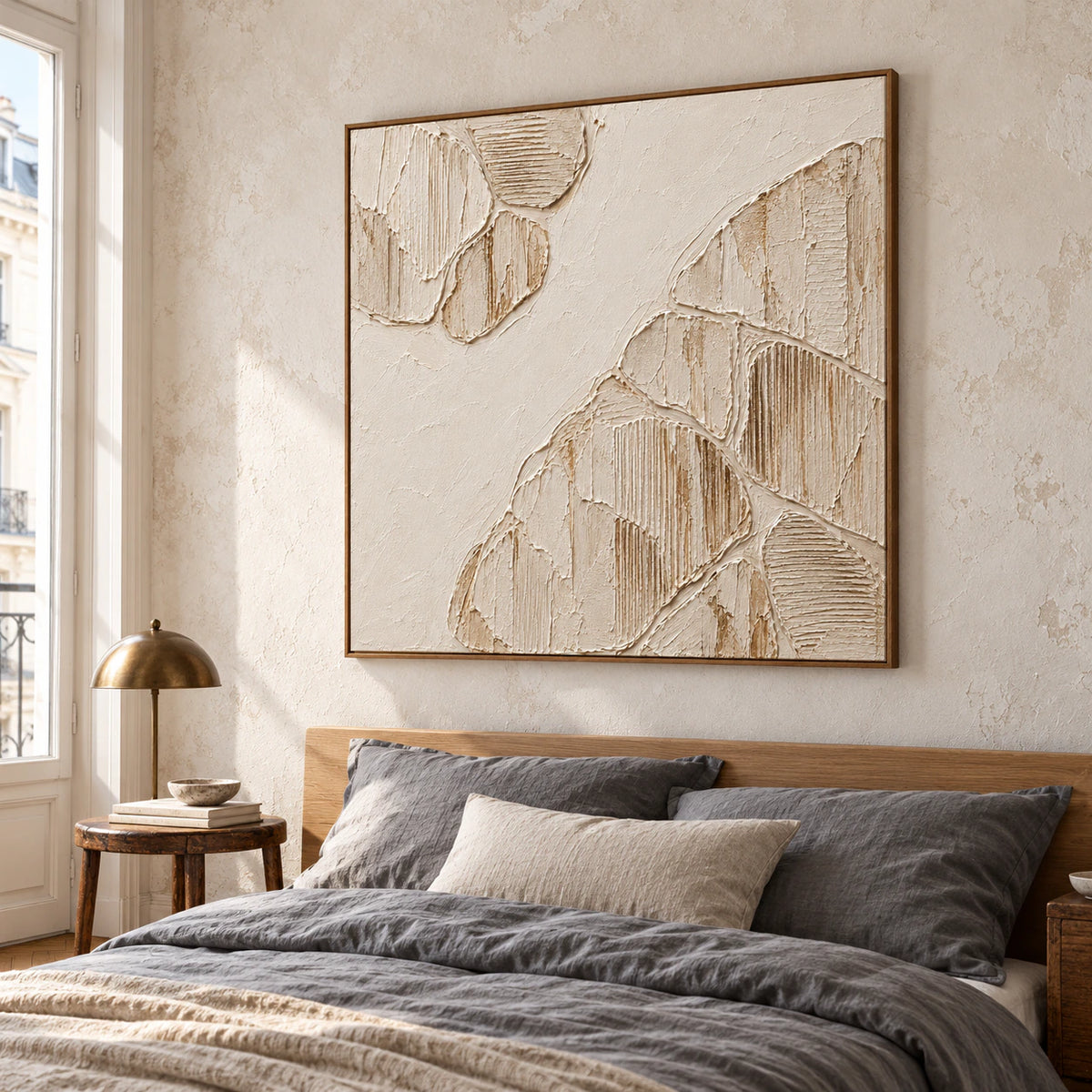 Large square ivory relief above a low oak bed in a quiet, daylight-filled bedroom with muted gray linens.