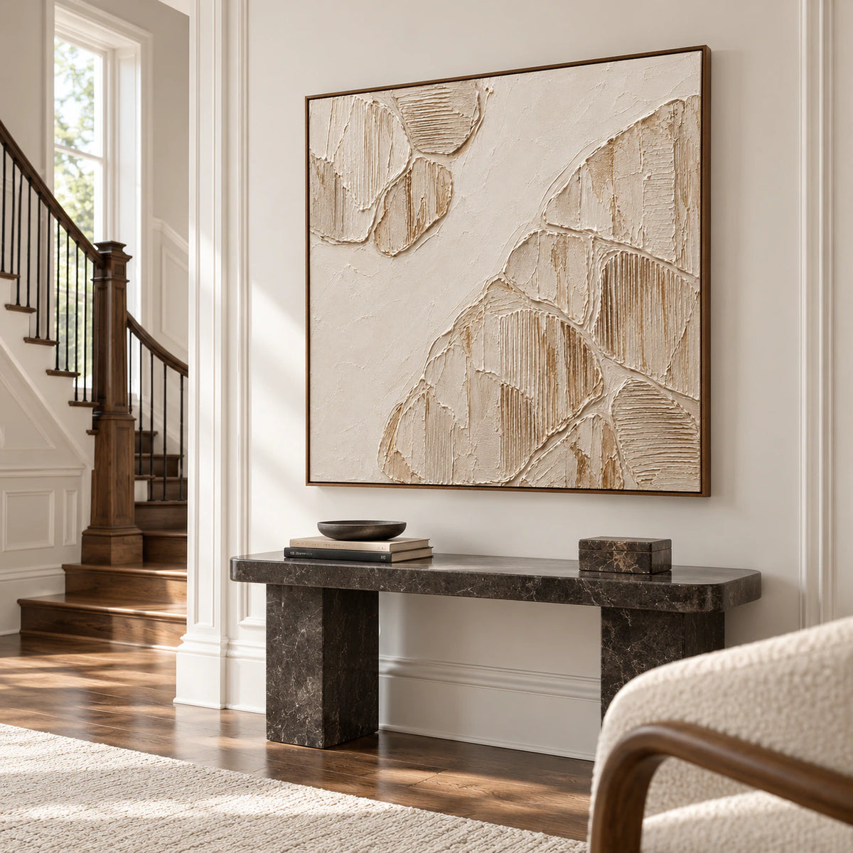 Large square ivory relief commanding a bright, tall foyer wall, with a dark stone console and open architectural stair.