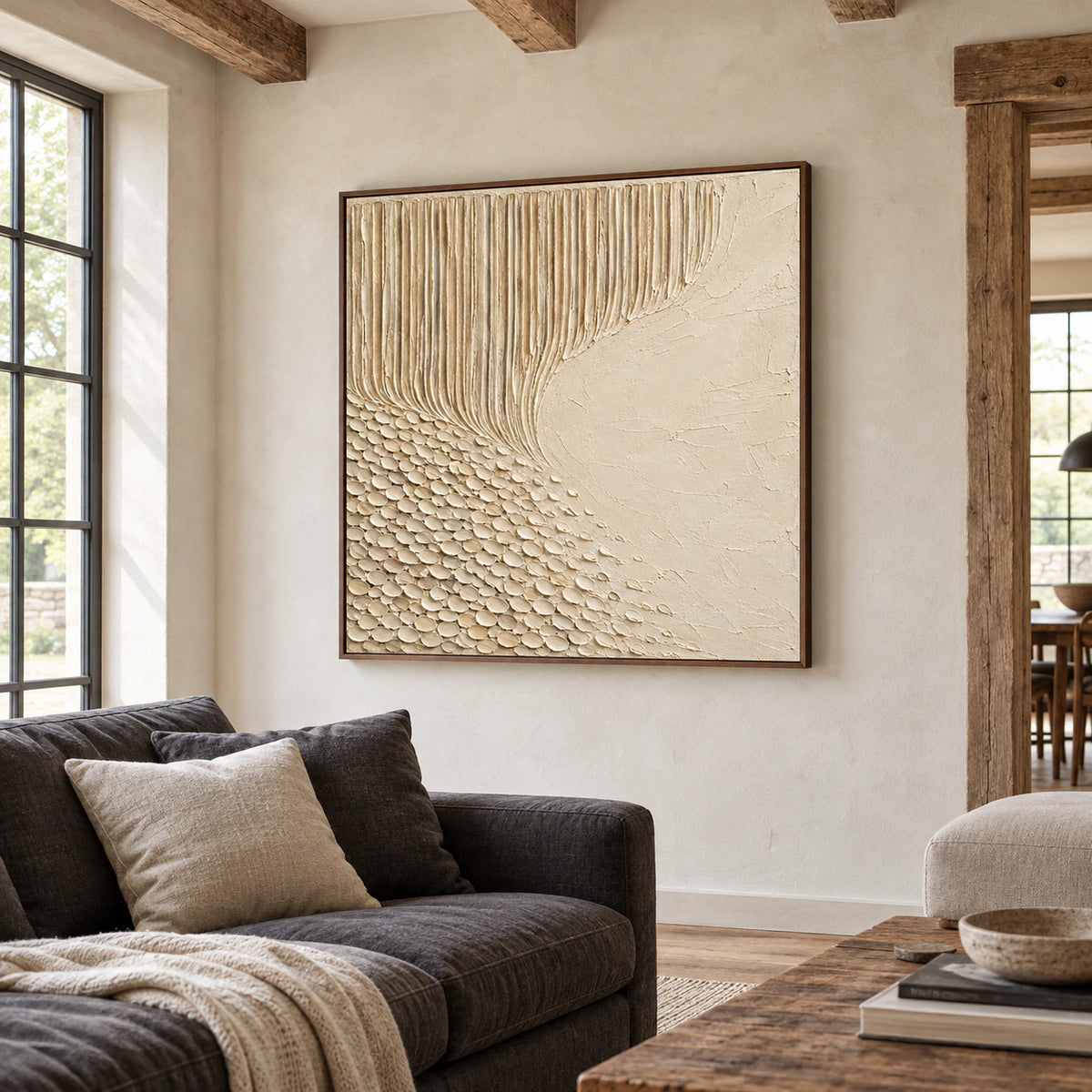 Large square ivory relief artwork above a charcoal sofa in a bright living room with pale walls and daylight.