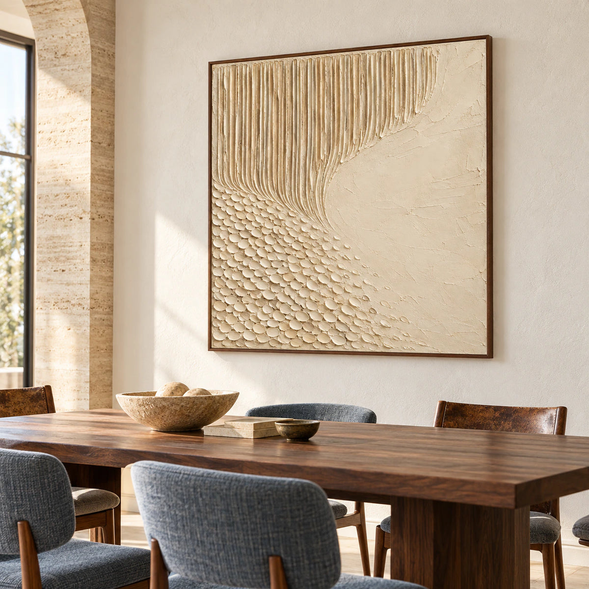 Square ivory relief artwork as the focal point of a refined dining room with dark wood table, linen chairs, and natural daylight.