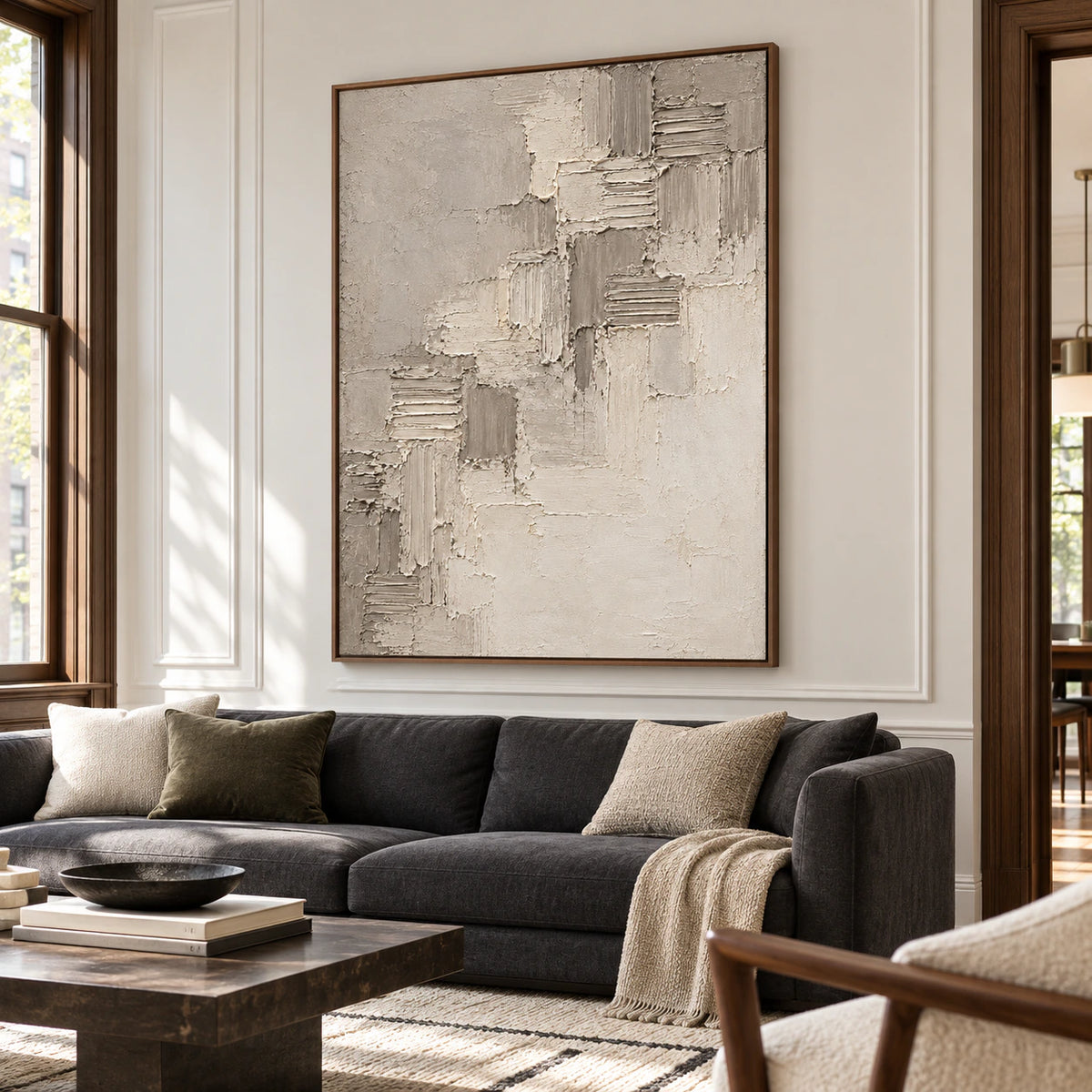 Riven-Cadence hangs prominently above a low charcoal sofa in a bright living room with pale walls and restrained furnishings.