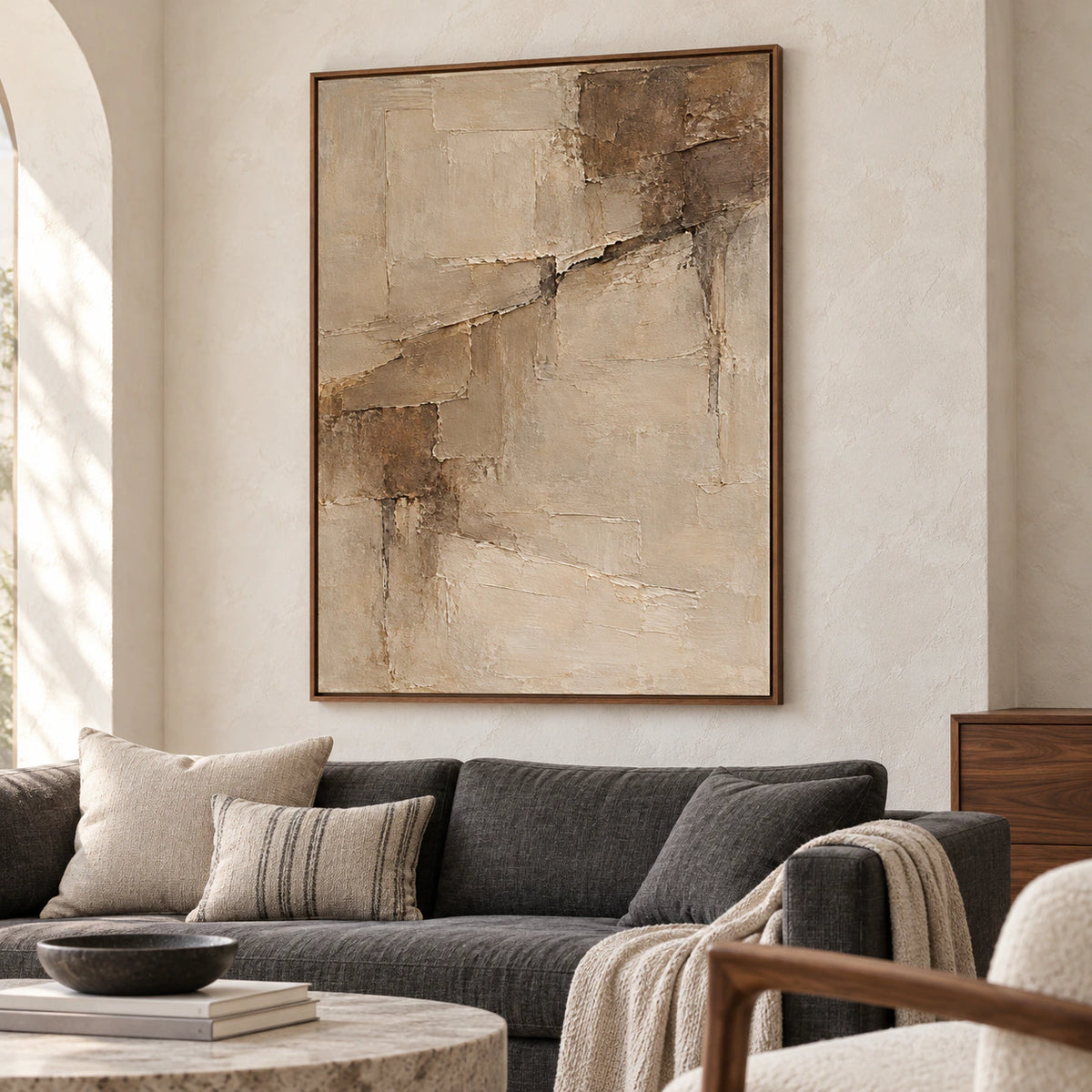 Riven-Parchment artwork above a restrained charcoal sofa in a bright living room with pale walls and generous daylight.