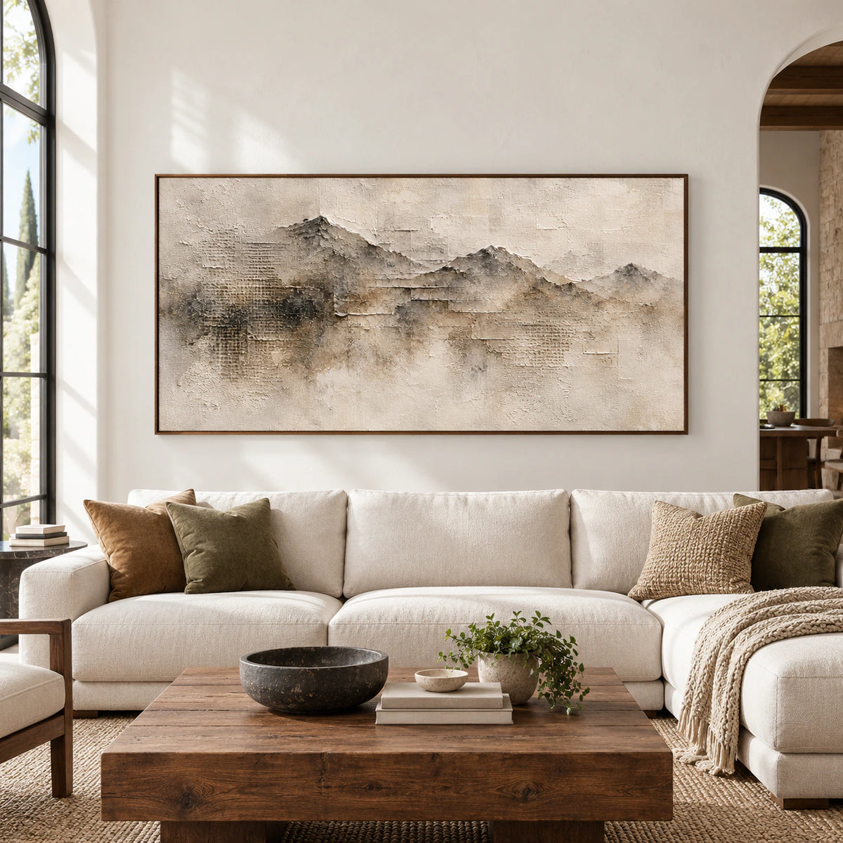 Panoramic ridgeline painting above a sofa in a spacious, bright room with contrasting furnishings, viewed straight on in natural daylight.