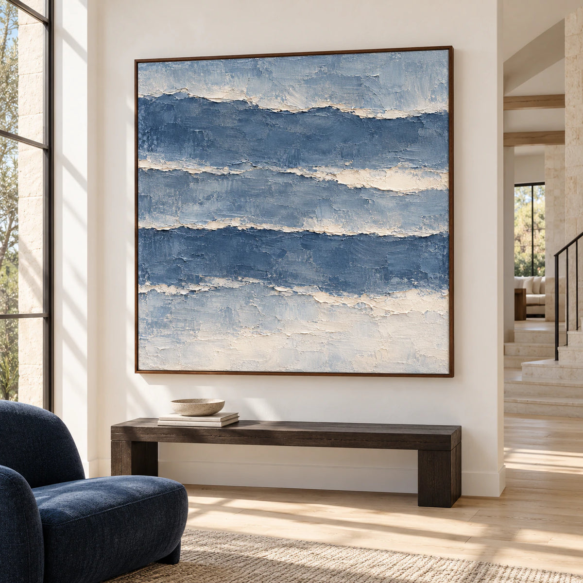 Riven-Tides painting above a dark bench against a light limestone wall in a bright foyer with wood flooring, viewed from a low left angle.