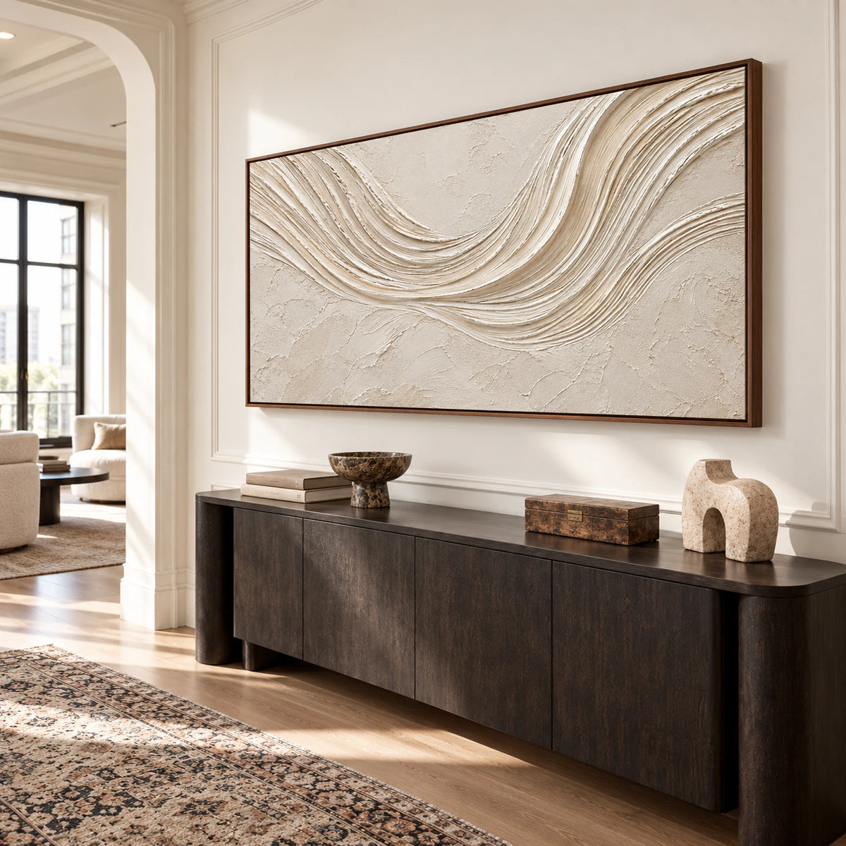 Slightly low, left oblique view of the ivory abstract painting on a warm white wall in a high-ceilinged foyer with a dark console and sculptural accents.