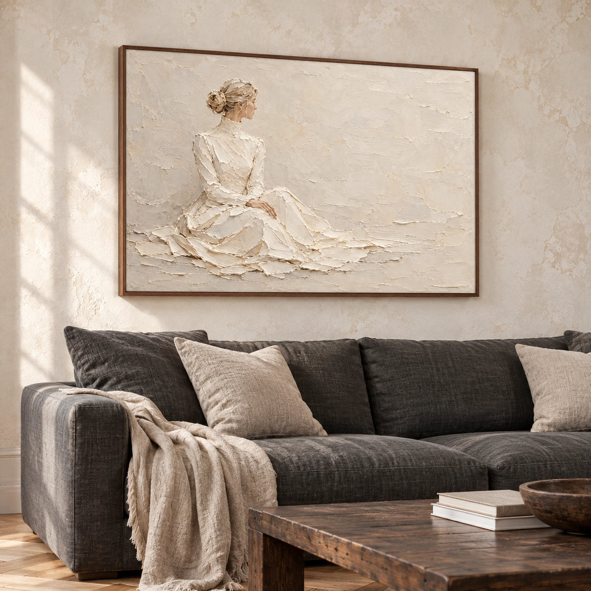 Large horizontal seated-figure artwork above a charcoal linen sofa in a bright living room with pale plaster walls and clear daylight.