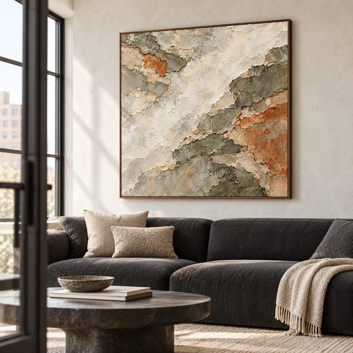 Large square Shale Traverse artwork above a low charcoal sofa in a bright living room with pale walls and daylight.