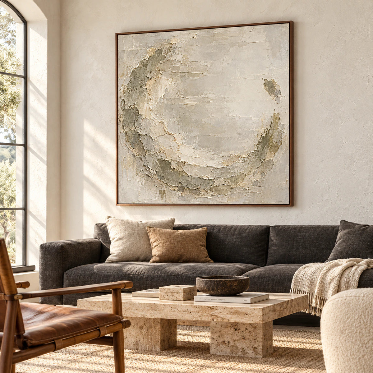 Large square textured painting above a charcoal sofa against a light plaster wall in a bright living room, viewed obliquely from the left.