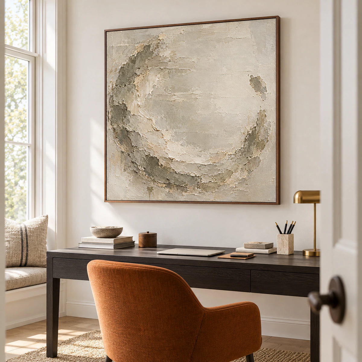 Square textured abstract painting above a dark desk in an airy office with tall windows and a reading chair, viewed from a low angle on the right.