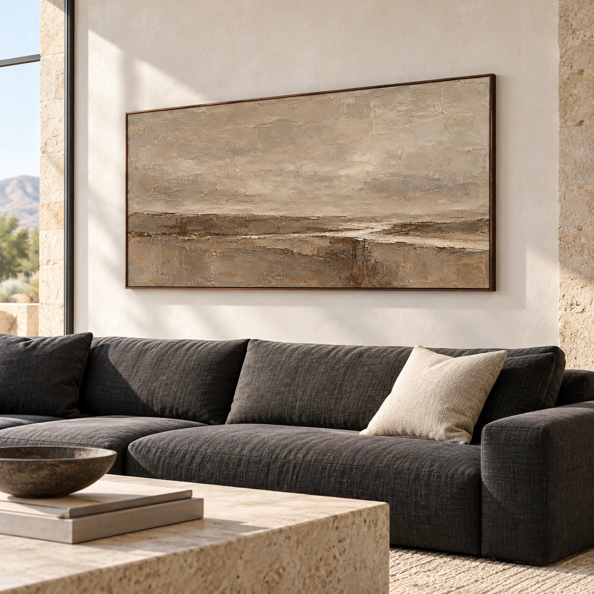 Large neutral abstract painting above a charcoal sofa against pale plaster walls in a bright living room, viewed at a gentle angle from the left.