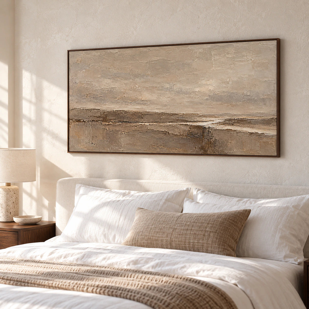 Sand and umber abstract painting above a light upholstered bed with white linen and walnut bedside furniture, viewed from an elevated left angle in soft morning light.