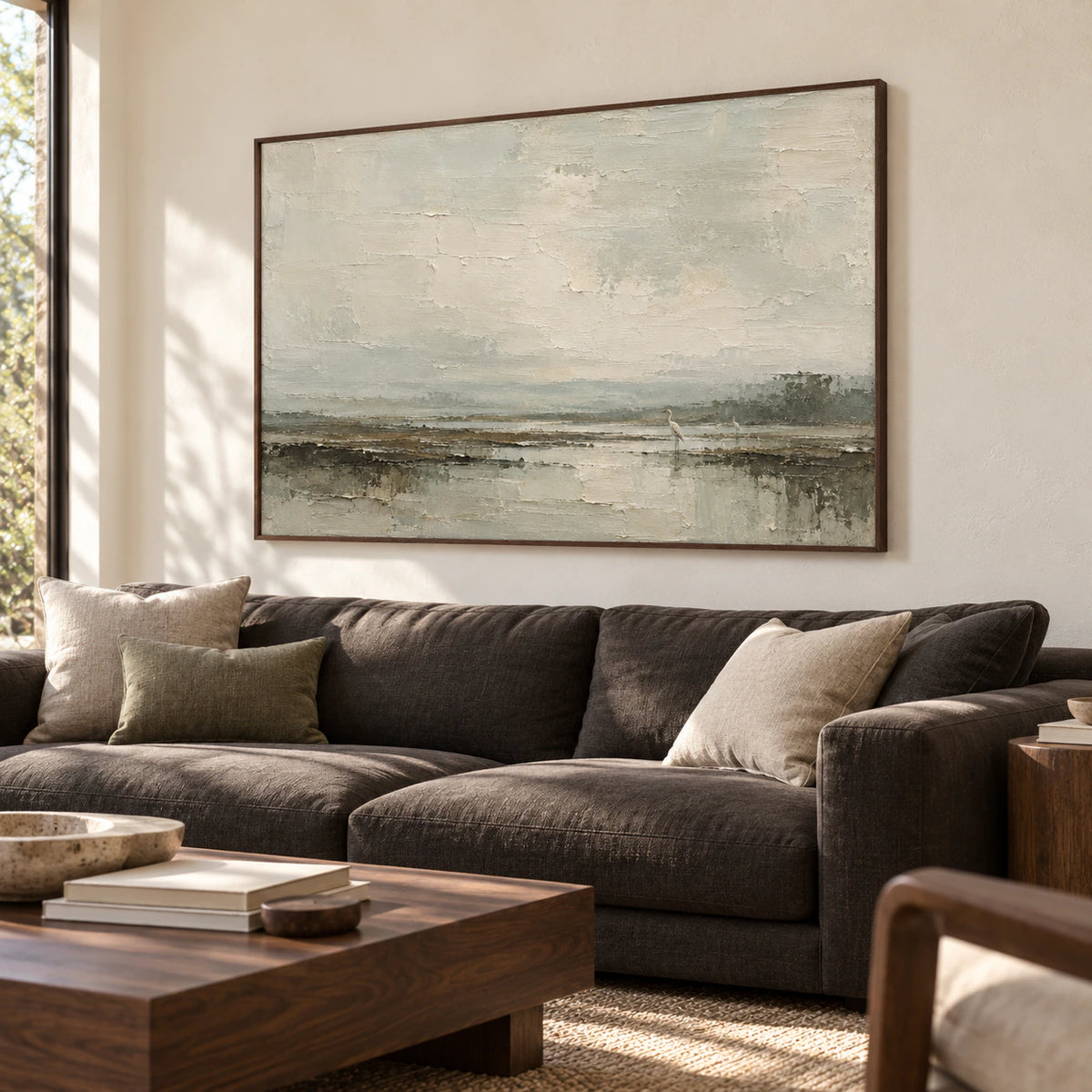 Large marsh artwork above a restrained charcoal sofa in a bright living room, its pale sky and two birds clearly visible.