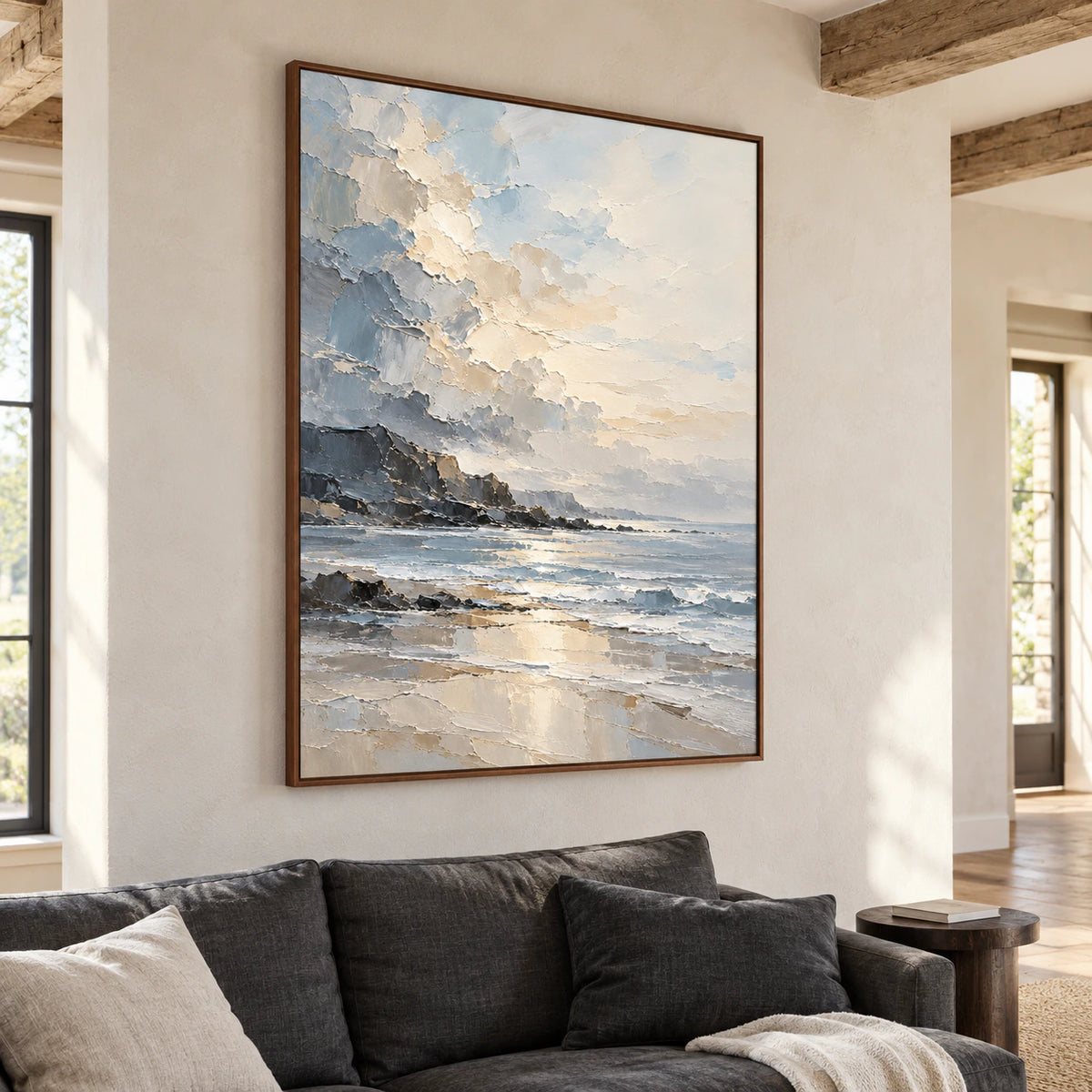 Vertical coastal painting above a low charcoal sofa, with a pale plaster wall, oak floor and dark side table, viewed from the left in natural daylight.