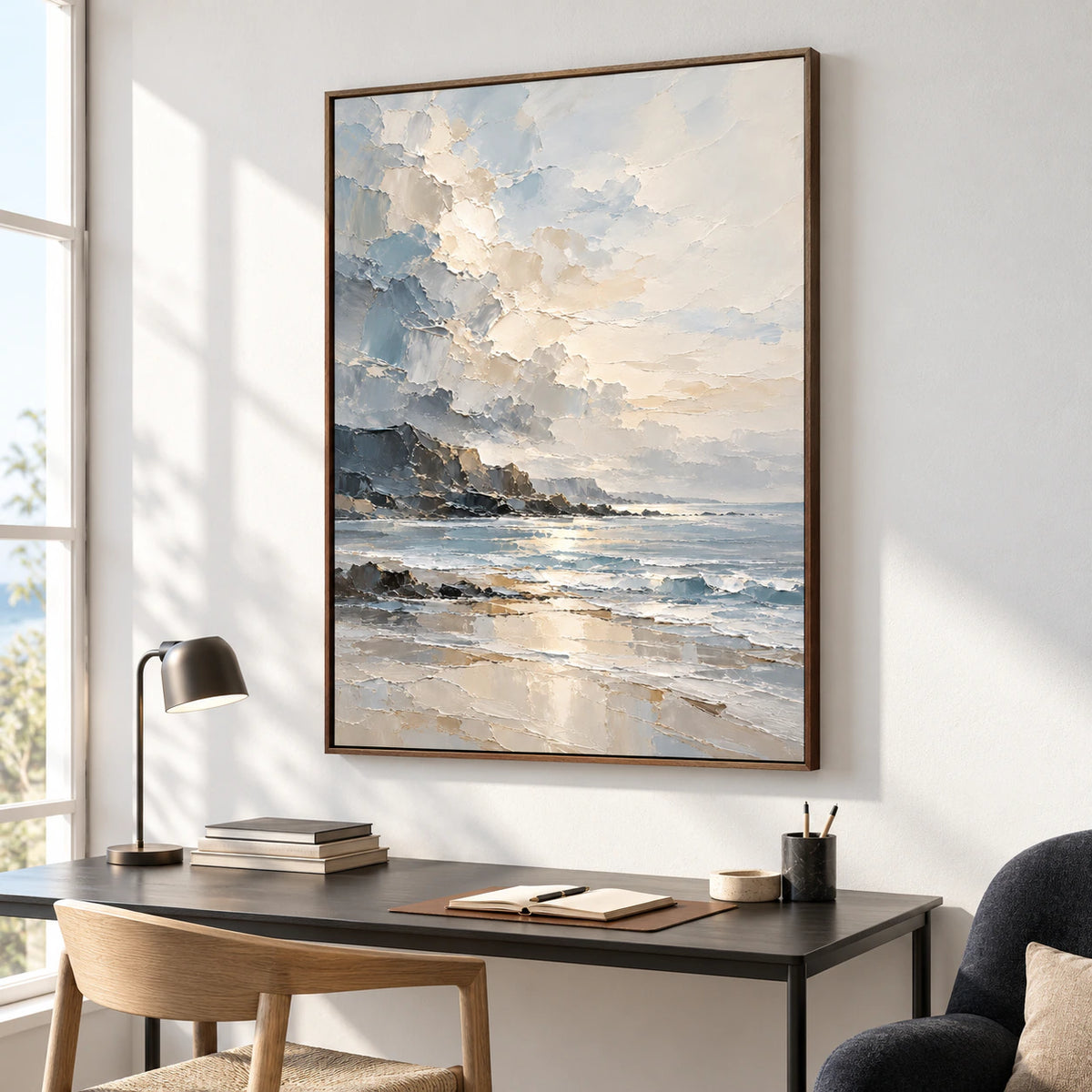 Coastal painting on a cool pale wall beside a slim black desk, warm wood chair and small reading lamp, viewed from the right in window daylight.