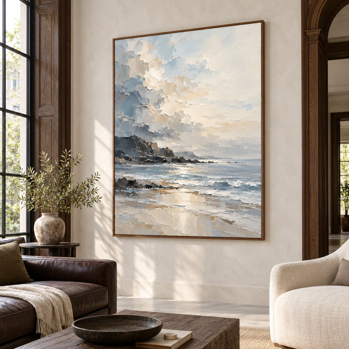 Coastal painting on a warm white wall in a spacious hospitality loft with tall industrial windows, a dark leather banquette and pale concrete flooring, viewed from the right.
