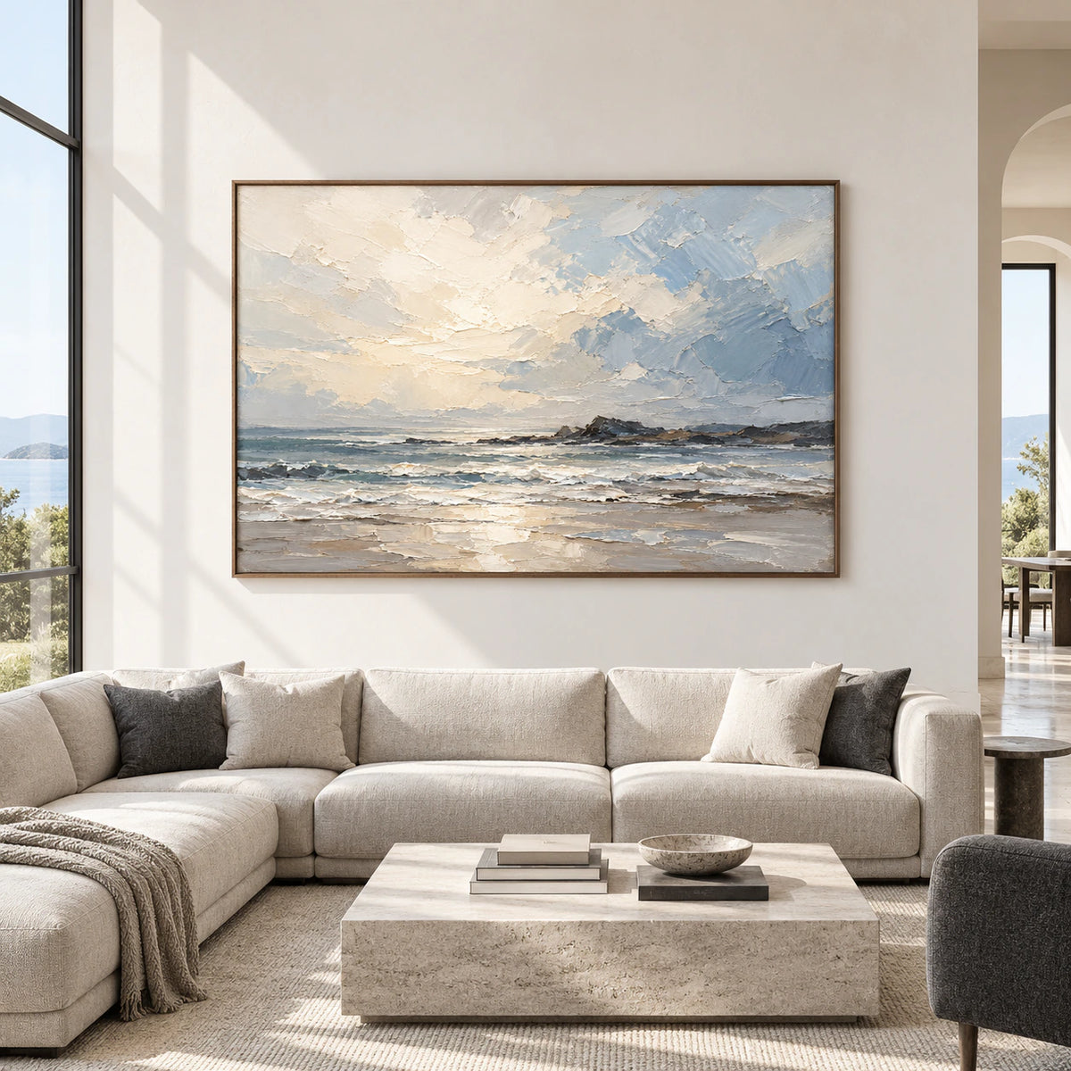 Straight-on view of a large horizontal seascape painting in a bright, open living room with charcoal and pale stone furnishings.