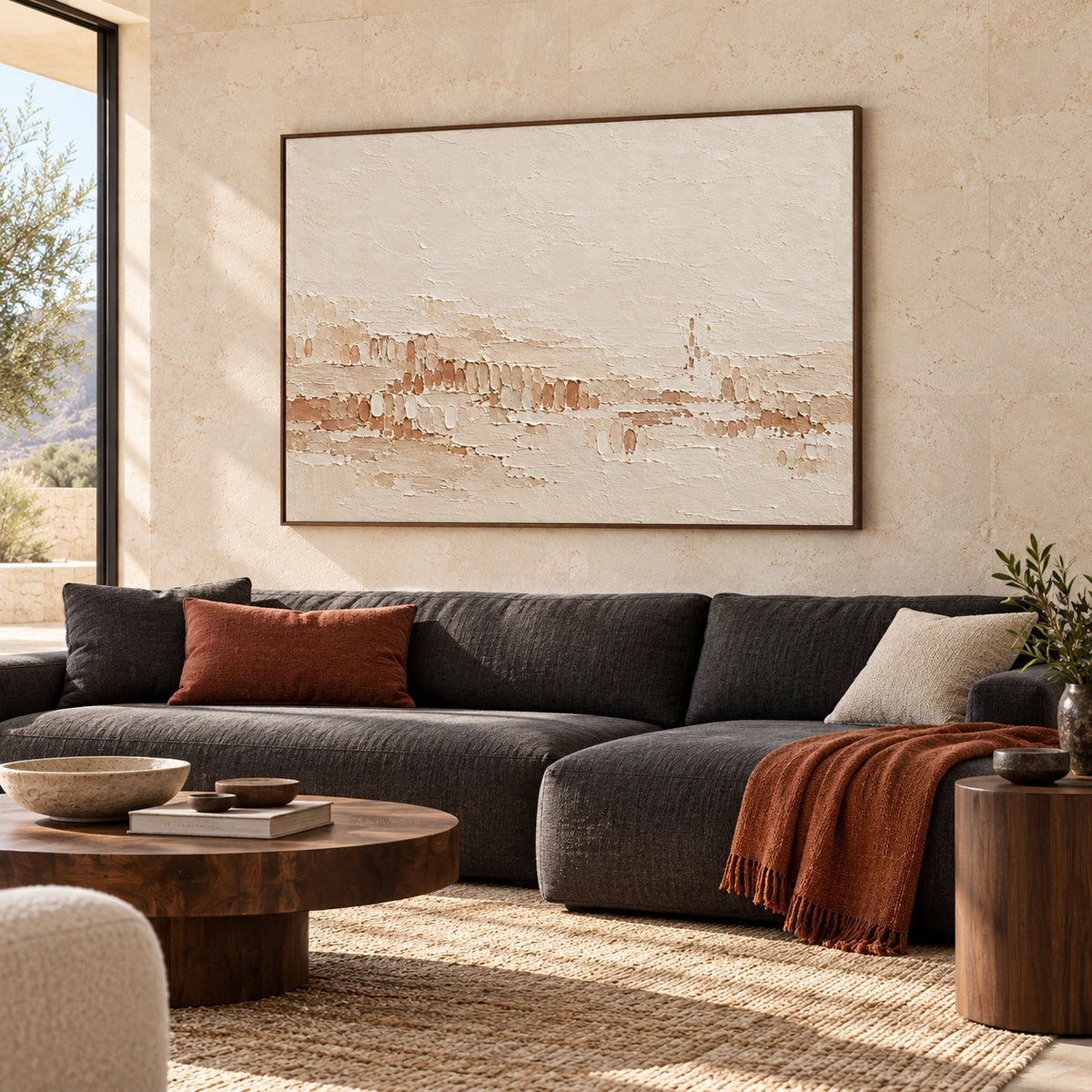 Tonal-Stitch artwork above a low charcoal sofa in a bright living room with pale stone walls and natural daylight.