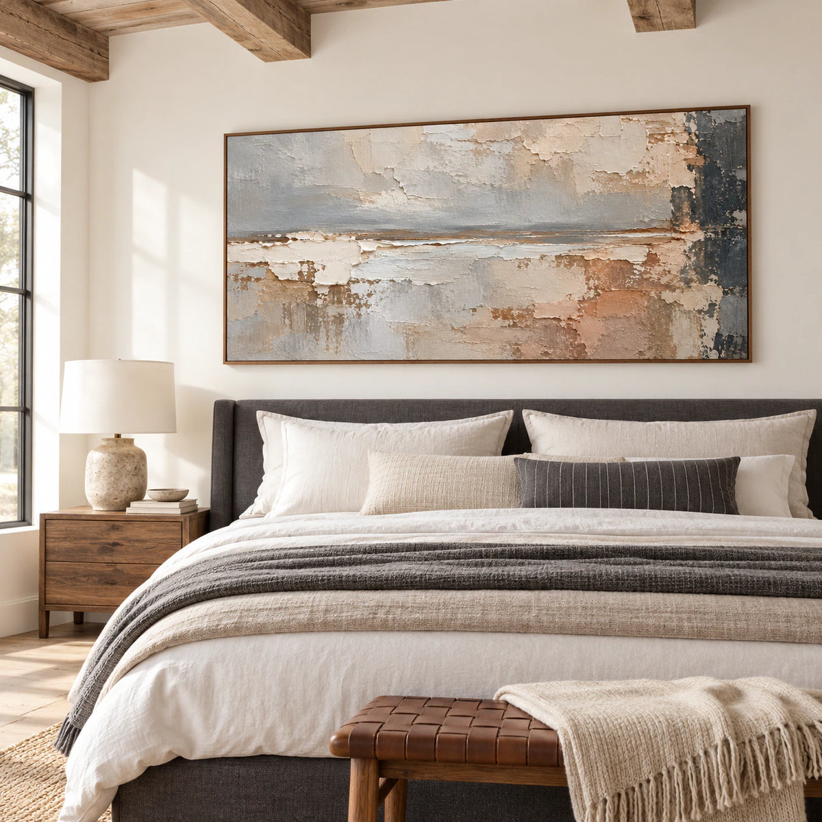 Large horizontal abstract painting above a charcoal upholstered bed in a bright bedroom, viewed at a slight oblique angle in soft morning daylight.