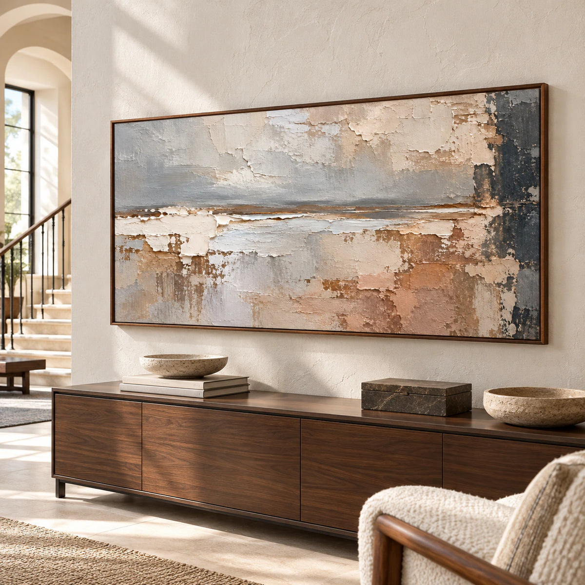 Large horizontal abstract painting on a tall light stone foyer wall above a low dark console, viewed from a right oblique angle in natural daylight.