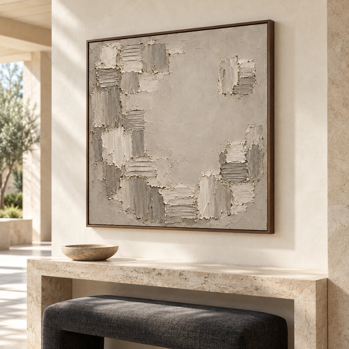 Torn-Mosaic fills the view above a console in a gallery-scale foyer, seen from the right at eye level with pale stone architecture, a dark bench and bright daylight.
