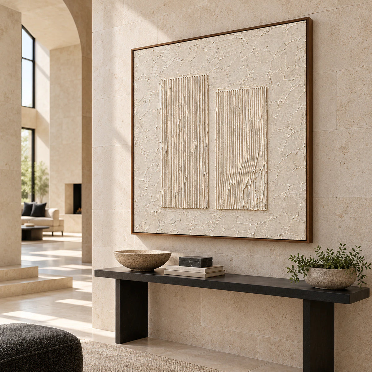 Left oblique view of large square ivory artwork above a slender black console on a cool limestone wall in a tall foyer lit by a high window.