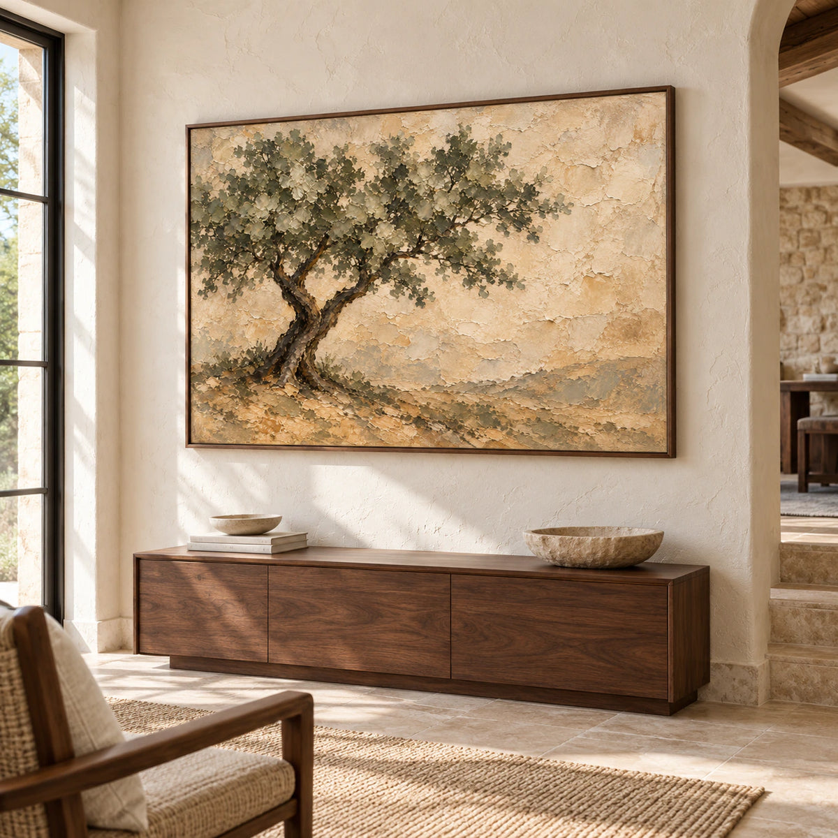 Large horizontal tree painting above a wood console cabinet in a bright foyer with a pale stone wall and broad stone floor.