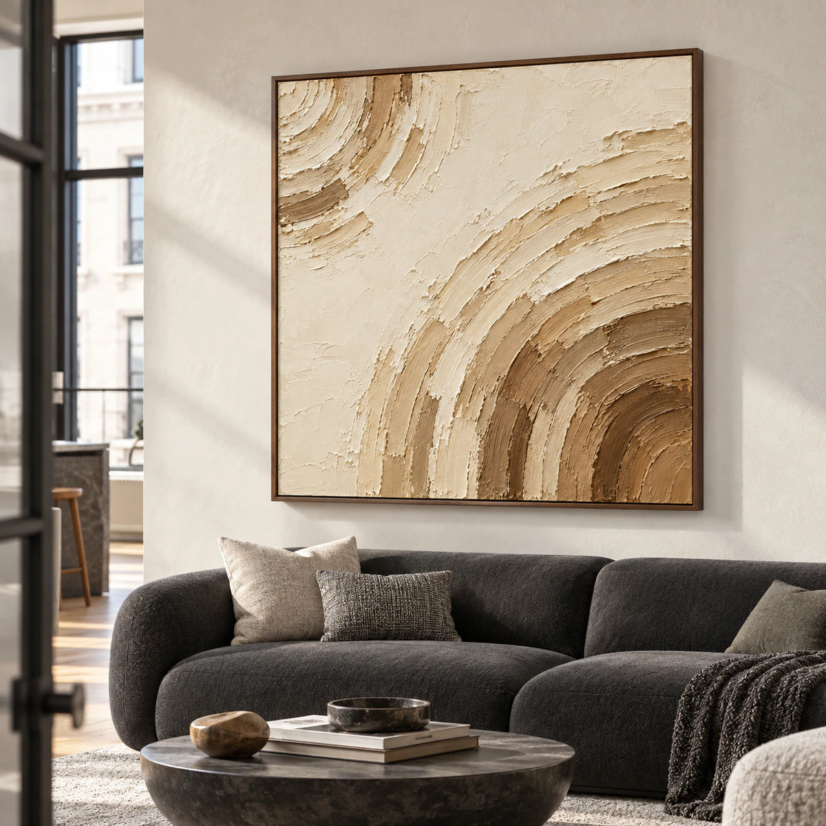 Square ivory and umber abstract painting above a charcoal sofa against light plaster walls, viewed from the left at seated eye level in a bright living room.