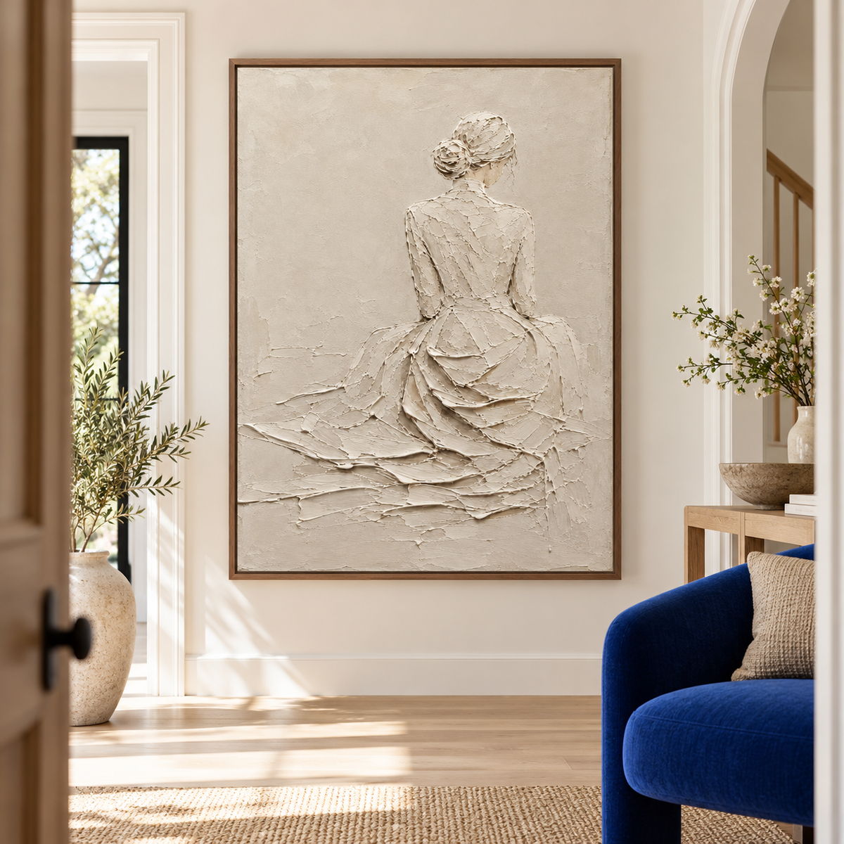 Low, slightly upward view from the left of a large ivory figure painting on a tall textured wall above a simple bench in a bright, spacious foyer.
