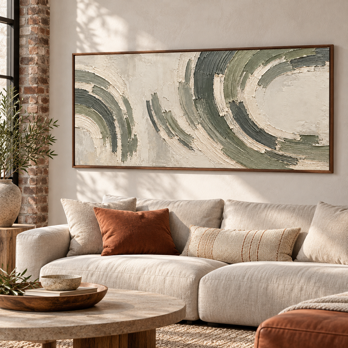 Left oblique view of a sage and charcoal abstract painting above a low pale upholstered sofa in a bright living room with light wood and a muted rust accent.