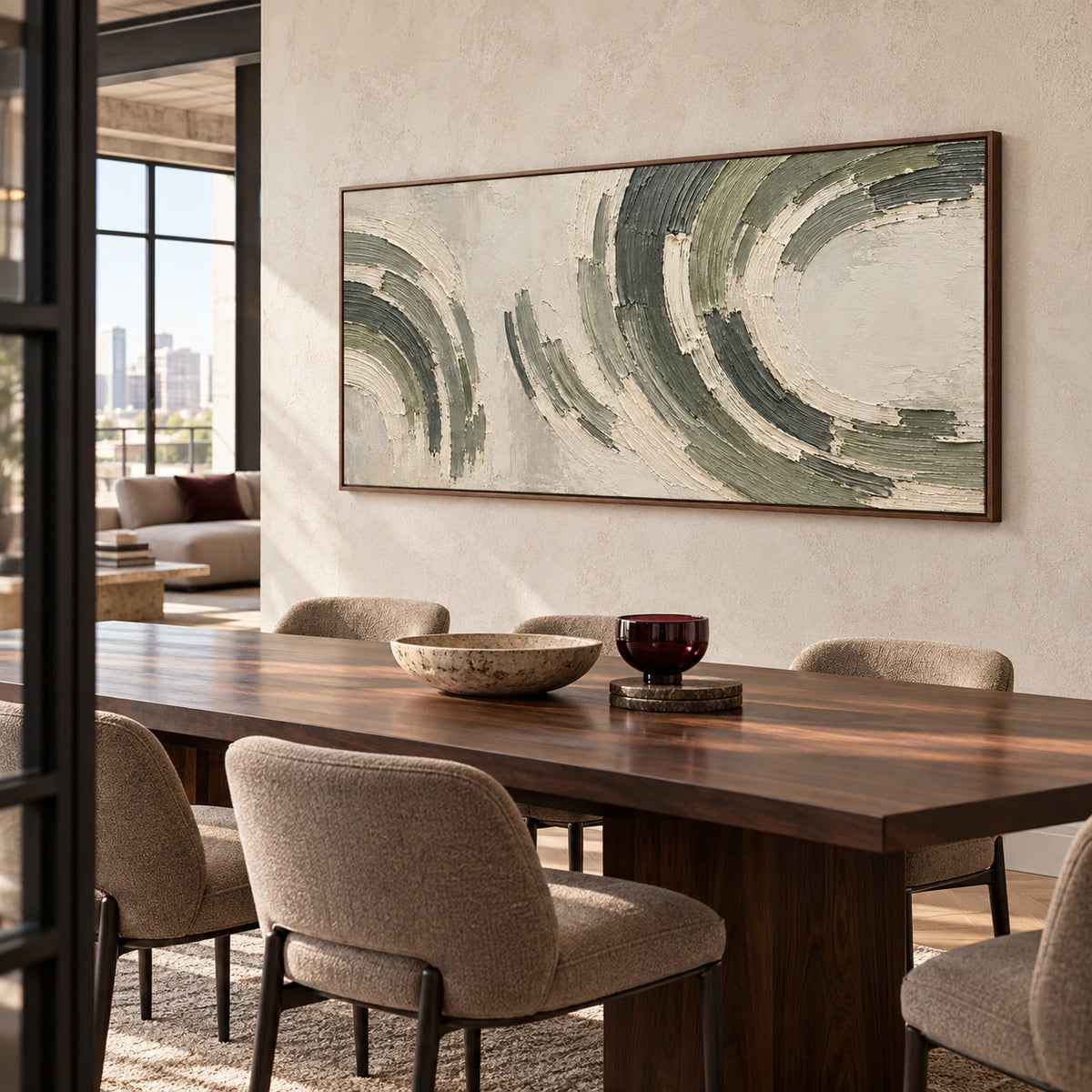 Right oblique view of the textured abstract painting on a light limestone wall above a dark walnut dining table with taupe chairs and a burgundy glass accent.