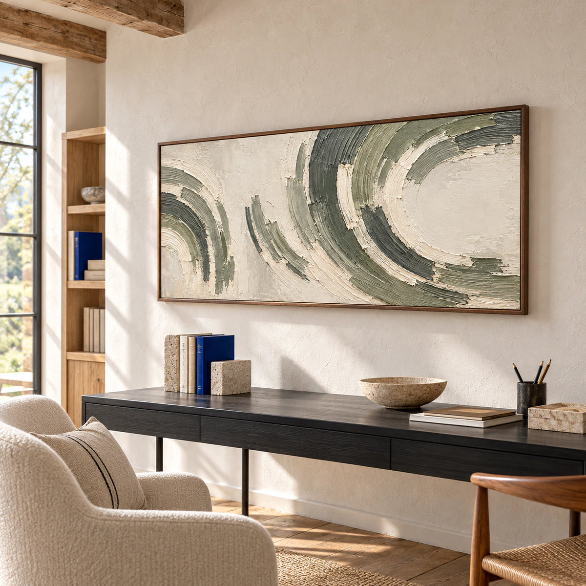 Elevated left oblique view of the abstract painting above a slender black desk beside an ivory reading chair, with light oak shelving and a cobalt book accent.